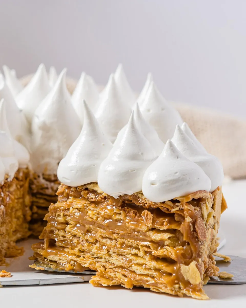 Corte de torta chilena mostrando decenas de capas de hojarasca con manjar y picos de merengue