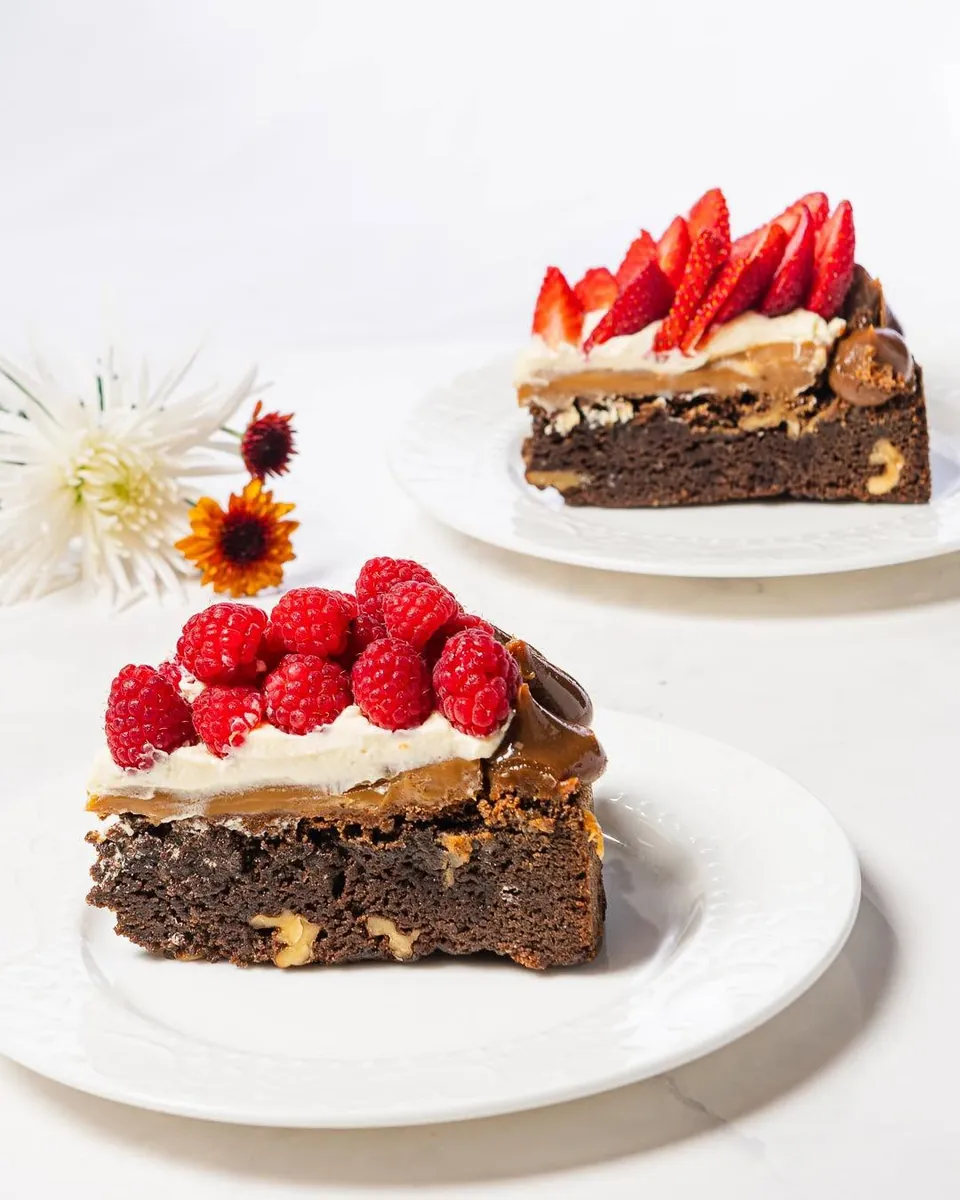 Dos porciones de brownie, una con fresas y otra con frambuesas, servidas en platos blancos