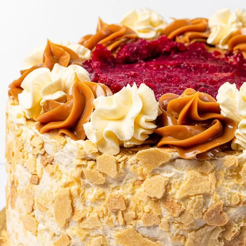 Torta mil hojas entera vista desde arriba con rosetones de crema y manjar y frambuesas al centro