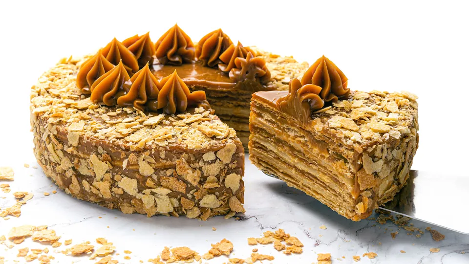 Torta chilena entera con rosetones de manjar y una porción levantada que muestra las capas de hojarasca